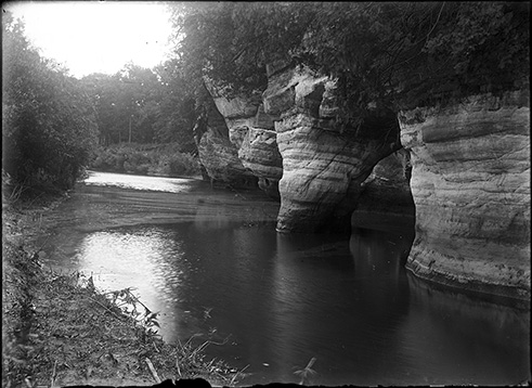 black and white photograph showing a river with sandstone bluffs along the bank